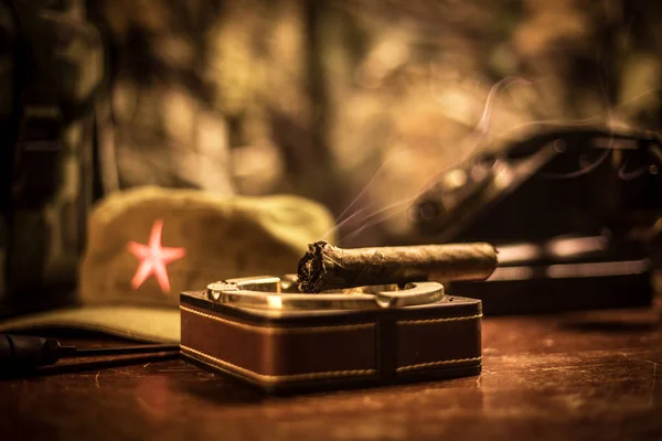 Feche um charuto e cinzeiro cubano na mesa de madeira. Mesa de comandante do ditador comunista na sala escura. Conceito de mesa de trabalho do general do exército . — Fotografia de Stock