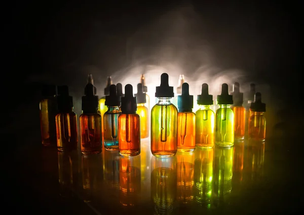 VAPE koncept. Kouřové mraky a lahvičky s tekutinou na tmavém pozadí. Světelné efekty. Užitečné jako pozadí nebo elektronická reklama na cigarety. — Stock fotografie