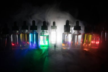 Elektronik sigara sıvısı ile dolu dev cam şişeler ile sisli bir gecede yolun ortasında duran bir adamın silueti. Arka planda ışık ile renkli sisli bulutlar.