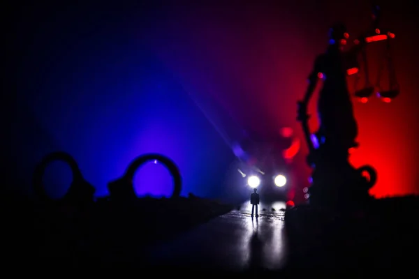 Legal law concept. Silhouette of handcuffs with The Statue of Justice on backside with the flashing red and blue police lights at foggy background. Selective focus — Stock Photo, Image
