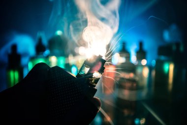 Vape kavramı. Elektronik Sigara vape patlaması. Duman bulutlar ve karanlık arka plan üzerinde vape sıvı şişeler. Işık efektleri. Vape reklam olarak yararlı.