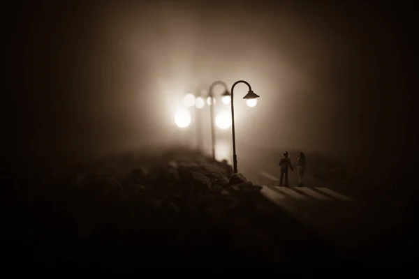 Casal jovem segurando as mãos um do outro. Caminhando lentamente sob luzes brancas de rua durante a noite. Tempo negro. Atmosfera pacífica em névoa. Ar enevoado . — Fotografia de Stock