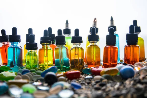 Concepto Vape. Hermosas botellas de vidrio líquido de vapor colorido al aire libre en piedras. Útil como fondo o publicidad electrónica de cigarrillos . — Foto de Stock