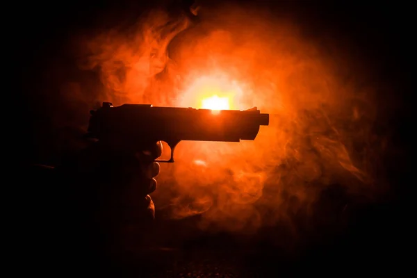 Pistola de mano masculina sobre fondo negro con luces traseras tonificadas con humo — Foto de Stock
