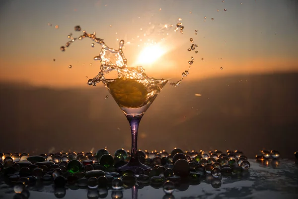 Martini cocktailglas i hand stänk på mörk tonad rökig bakgrund eller färggrann cocktail i glas med färgstänk och Oliver. Party club underhållning. Blandade ljus. Selektivt fokus — Stockfoto