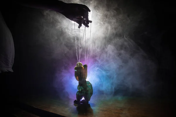 Concept of manipulation. Hand holds strings for manipulation. The hand controls the puppet strings on a dark foggy background.