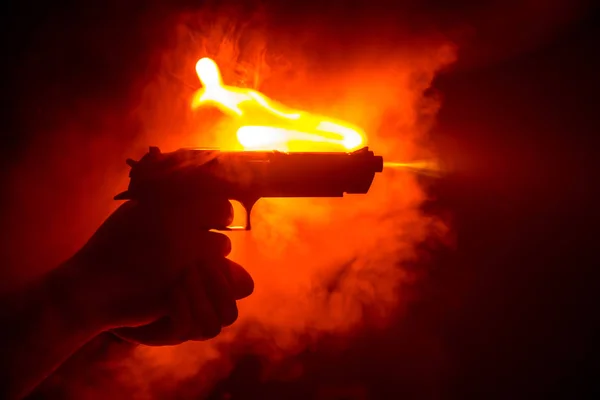 Male hand holding gun on black background with smoke toned back lights