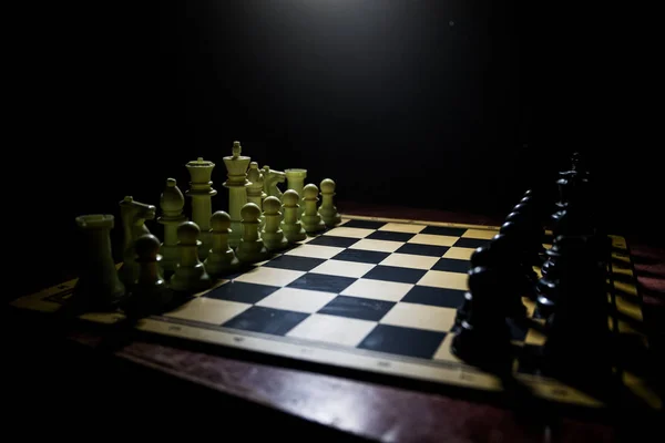 Schackbräde spel begreppet affärsidéer och konkurrens. Schack figurer på en mörk bakgrund med rök och dimma. — Stockfoto