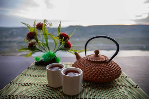 Te-konceptet. Japanska tea ceremoni kultur östra dryck. Tekanna och koppar på bordet med bambu löv på solnedgången — Stockfoto