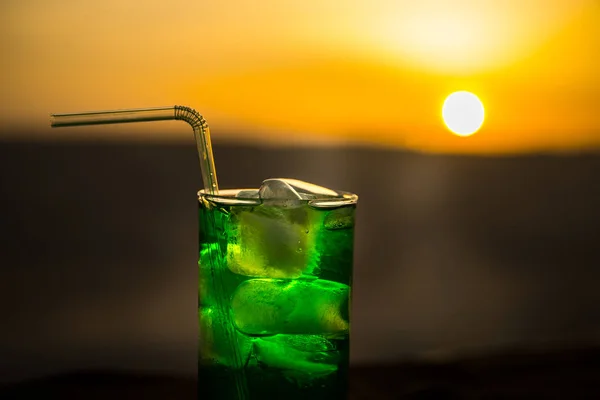Nahaufnahme nasses Glas grün kaltes Minzgetränk, farbenfroher orangefarbener Sonnenuntergang auf der Terrasse. kühlendes Sommergetränk. Sommer frisch und kühl Inspiration, Abend Kontrast Farbkombination. — Stockfoto