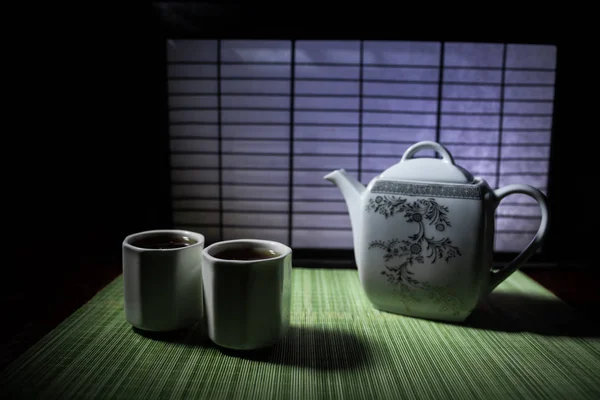 Tea concept. Japanese tea ceremony culture east beverage. Teapot and cups on table with bamboo leaves on sunset — Stock Photo, Image