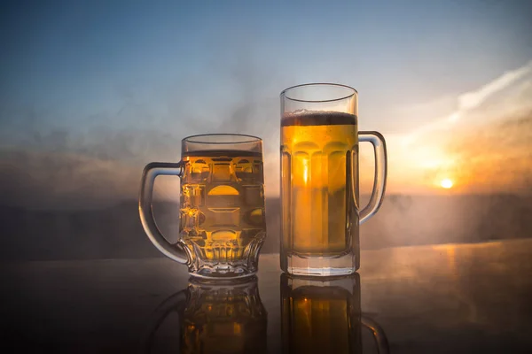 夕暮れ時のビーチでビールを飲みながら。クーリングサマードリンクコンセプト。太陽光の背景のボケでドラフトビールのグラスのクローズアップ — ストック写真