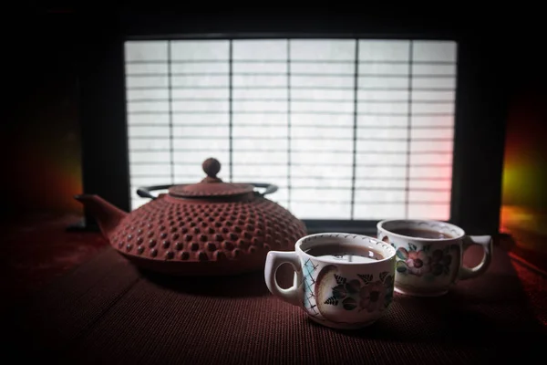 차 개념입니다. 일본 다도 문화 동쪽 음료. 석양을 바라보며 대나무 잎을 곁들인 테이블 위의 찻주전자와 컵 — 스톡 사진
