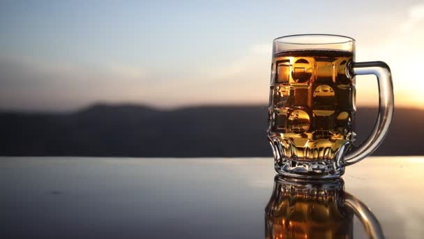 夕暮れ時のビーチでビールのグラス クーリングサマードリンクコンセプト 太陽光の背景 ソフトフォーカスのボケでドラフトビールのグラスのクローズアップ — ストック動画