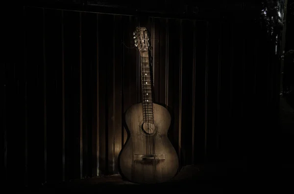 An wooden acoustic guitar is against a grunge textured wall. The room is dark with a spotlight for your copyspace.