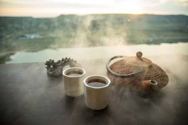 Te-konceptet. Japanska tea ceremoni kultur östra dryck. Tekanna och koppar på bordet med bambu löv på solnedgången — Stockfoto