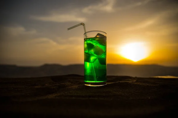 Close up wet glass of green cold mint drink, colorful orange sunset background on the terrace. Cooling summer drink. Summer fresh and cooling inspiration, evening contrast color combination.