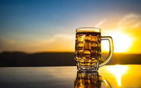 Bicchiere di birra su una spiaggia al tramonto. Raffreddamento concetto di bevanda estiva. Close Up di un bicchiere di birra alla spina con il Bokeh di sfondo luce solare — Foto Stock