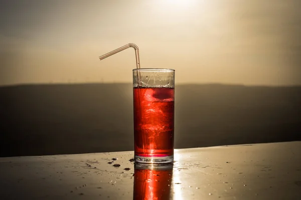 Cooling summer drink concept. Cocktail glasses splashing on sunset. Close up wet glass of cold drink on the terrace.