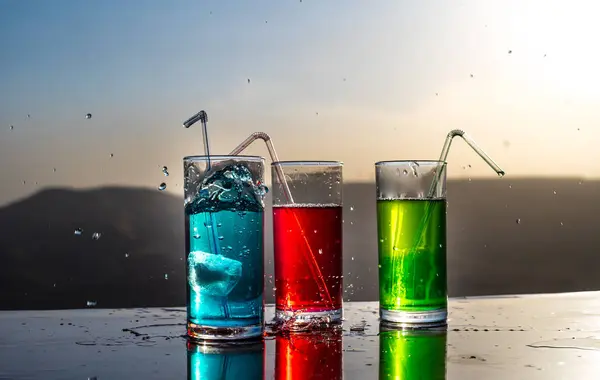 Cooling summer drink concept. Cocktail glasses splashing on sunset. Close up wet glass of cold drink on the terrace. — Stock Photo, Image