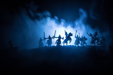 Süvari ve piyade ile Ortaçağ savaş sahnesi. Ayrı nesneler olarak figürlerin siluetleri, ortaçağ kalesi ile karanlık tonda sisli arka plan üzerinde savaşçılar arasında mücadele.