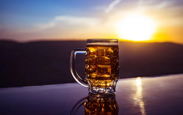 Bicchiere di birra su una spiaggia al tramonto. Raffreddamento concetto di bevanda estiva. Close Up di un bicchiere di birra alla spina con il Bokeh di sfondo luce solare — Foto Stock