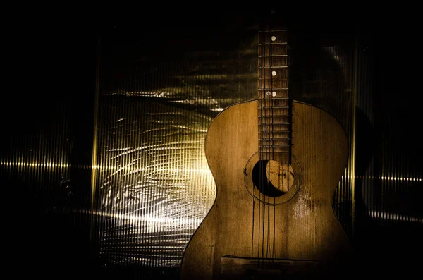 An wooden acoustic guitar is against a grunge textured wall. The room is dark with a spotlight for your copyspace. — Stock Photo, Image