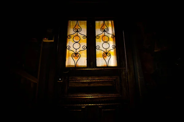 Silhueta de uma figura de sombra desconhecida em uma velha porta de madeira através de uma porta de vidro fechada. A silhueta de um humano à frente de uma janela à noite . — Fotografia de Stock