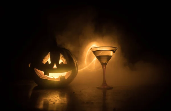 Cocktail di arancia zucca Halloween. Bevanda festiva. Festa di Halloween. Zucca divertente con un bicchiere da cocktail incandescente su uno sfondo scuro tonico nebbioso . — Foto Stock