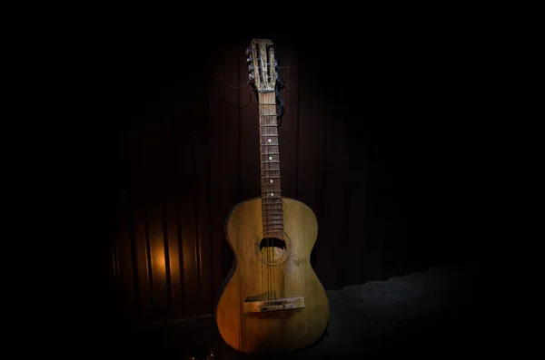 An wooden acoustic guitar is against a grunge textured wall. The room is dark with a spotlight for your copyspace. — Stock Photo, Image
