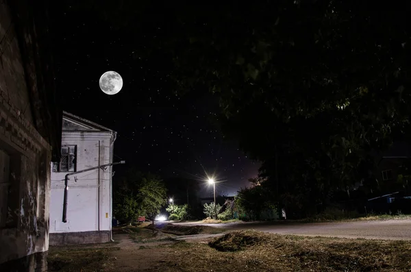Luna llena sobre un pueblo tranquilo por la noche. Hermoso paisaje nocturno de la calle del casco antiguo con luces. Rusia — Foto de Stock