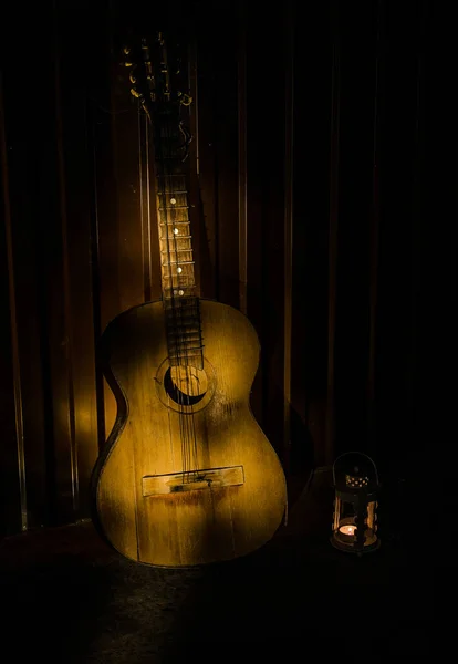 一把木制的原声吉他靠在一面有纹理的墙壁上。房间很暗,有聚光灯,适合您的复制空间. — 图库照片