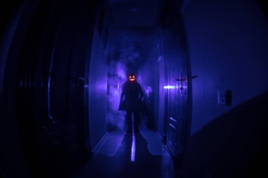 Cadılar Bayramı konsepti. Balkabağı başlı karanlık koridorda ürpertici siluet. Arka planda sis olan tonlu ışık. Seçici odaklama