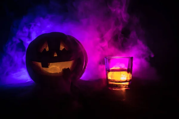 Halloween pompoen met gesneden gezicht en glas whiskey met ijs op een donker getinte mistige achtergrond met zombies. Ingericht. Selectieve aandacht — Stockfoto