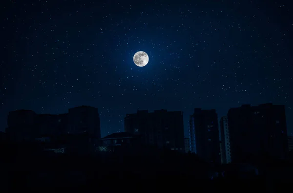 Silhuetas de arranha-céus construção diferente na cidade escura com fundo de uma grande lua — Fotografia de Stock