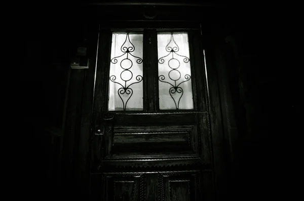 Silhouette d'une silhouette d'ombre inconnue sur une vieille porte en bois par une porte vitrée fermée. La silhouette d'un humain devant une fenêtre la nuit . — Photo