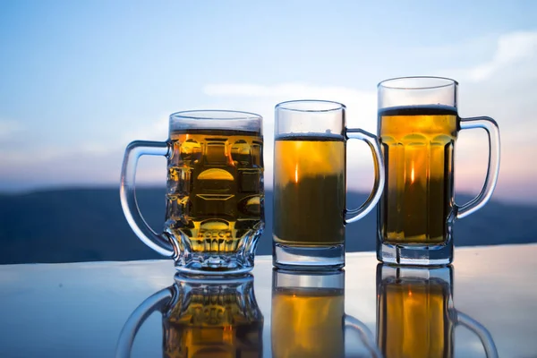 Glass of beer on a beach at sunset. Cooling summer drink concept. Close Up of A Glass of Draught Beer with the Bokeh of Sunlight Background