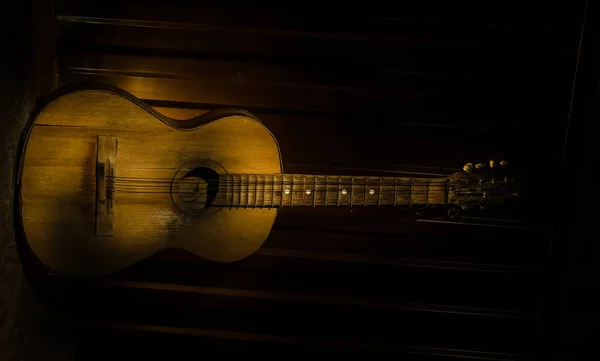 An wooden acoustic guitar is against a grunge textured wall. The room is dark with a spotlight for your copyspace.