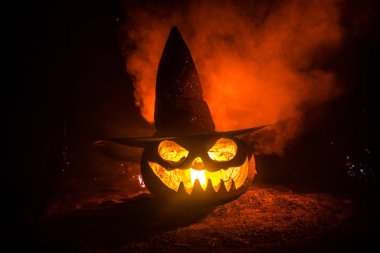 Cadılar Bayramı konsepti. Jack-o-fener gülümseme ve parti gece için korkutucu gözleri. Karanlık sisli arka planda cadı şapkası ile korkunç kabak yakından görünümü. Seçici odaklama.