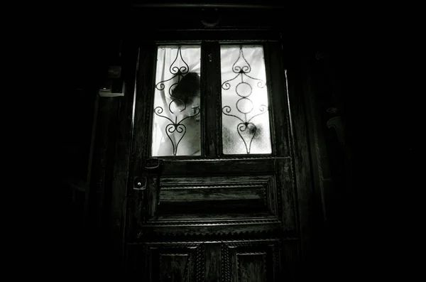 Silhouette of an unknown shadow figure on a old wooden door through a closed glass door. The silhouette of a human in front of a window at night. — Stock Photo, Image