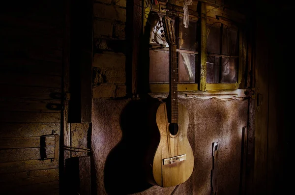 Une guitare acoustique en bois est contre un mur texturé. La pièce est sombre avec un projecteur pour votre copyspace . — Photo