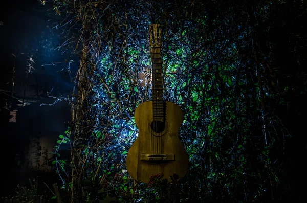 An wooden acoustic guitar is against a grunge textured wall. The room is dark with a spotlight for your copyspace.