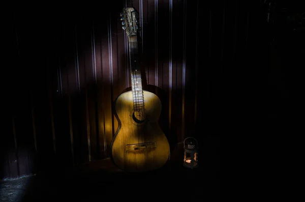 Une guitare acoustique en bois est contre un mur texturé. La pièce est sombre avec un projecteur pour votre copyspace . — Photo