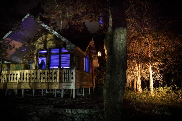 Casa velha com um fantasma na floresta à noite ou Abandonada Haunted Horror House no nevoeiro. Um velho edifício místico numa floresta de árvores mortas. Árvores à noite com lua. Luzes surreais. Conceito de Halloween horrível — Fotografia de Stock