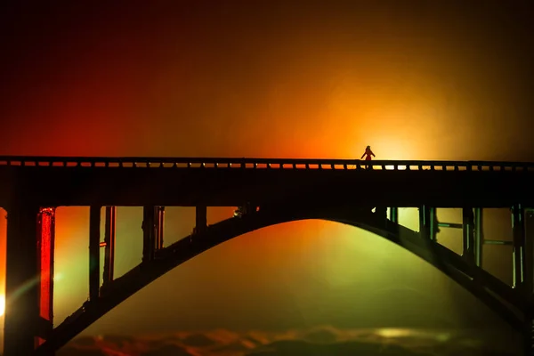 Decoración de obra. Silueta de puente metálico de gran alcance en la noche con contraluz nebulosa. Silueta de la persona de pie en el puente . — Foto de Stock