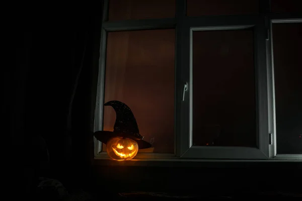 Calabaza de Halloween miedo en la ventana de la casa mística por la noche o calabaza de Halloween en la noche en la habitación con ventana azul. Símbolo de halloween en ventana . — Foto de Stock