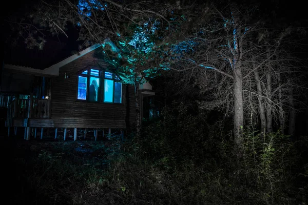 Old house with a Ghost in the forest at night or Abandoned Haunted Horror House in fog. Old mystic building in dead tree forest. Trees at night with moon. Surreal lights. Horror Halloween concept — Stock Photo, Image