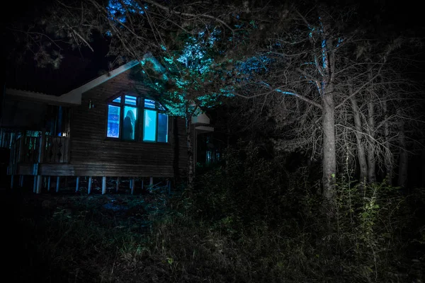 Casa velha com um fantasma na floresta à noite ou Abandonada Haunted Horror House no nevoeiro. Um velho edifício místico numa floresta de árvores mortas. Árvores à noite com lua. Luzes surreais. Conceito de Halloween horrível — Fotografia de Stock