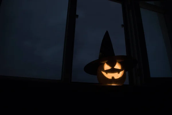 Scary Halloween pumpkin in the mystical house window at night or halloween pumpkin in night on room with blue window. Symbol of halloween in window.