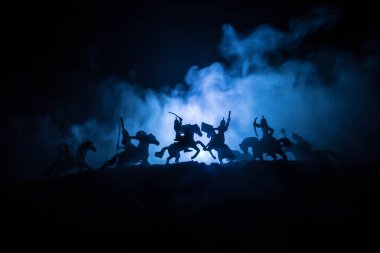 Süvari ve piyade ile Ortaçağ savaş sahnesi. Ayrı nesneler olarak figürlerin siluetleri, ortaçağ kalesi ile karanlık tonda sisli arka plan üzerinde savaşçılar arasında mücadele.